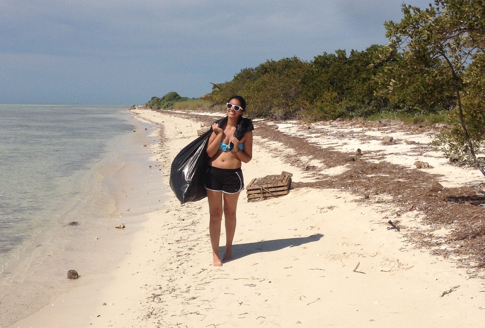 Girl carries trash bag off a beach.
