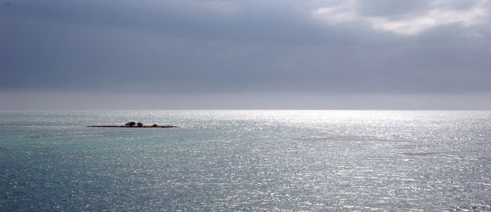 Photo of sky and sea with small island in mid-ground.